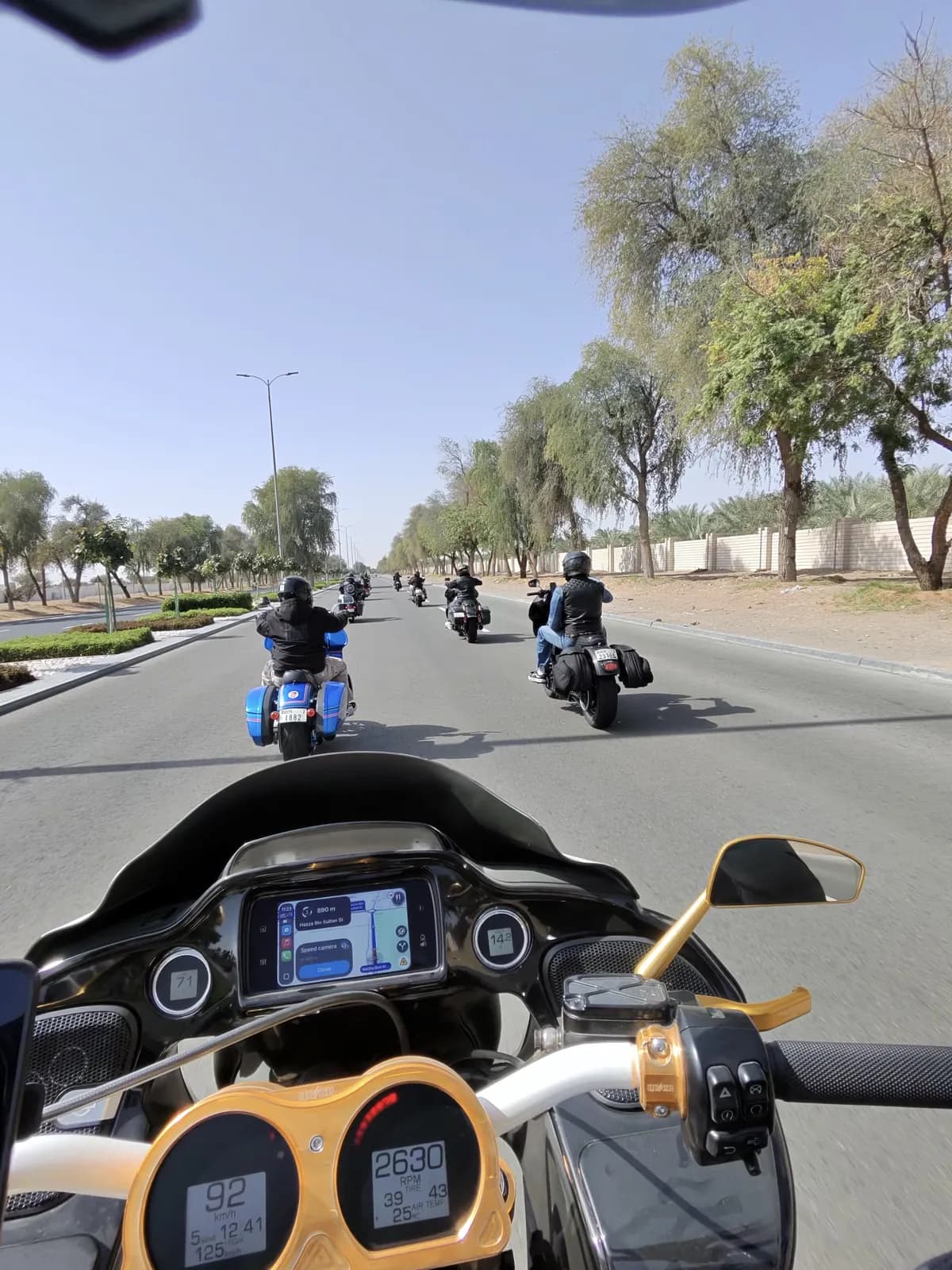Rider-eye view from a bagger cockpit following the group ride down a tree-lined Dubai road
