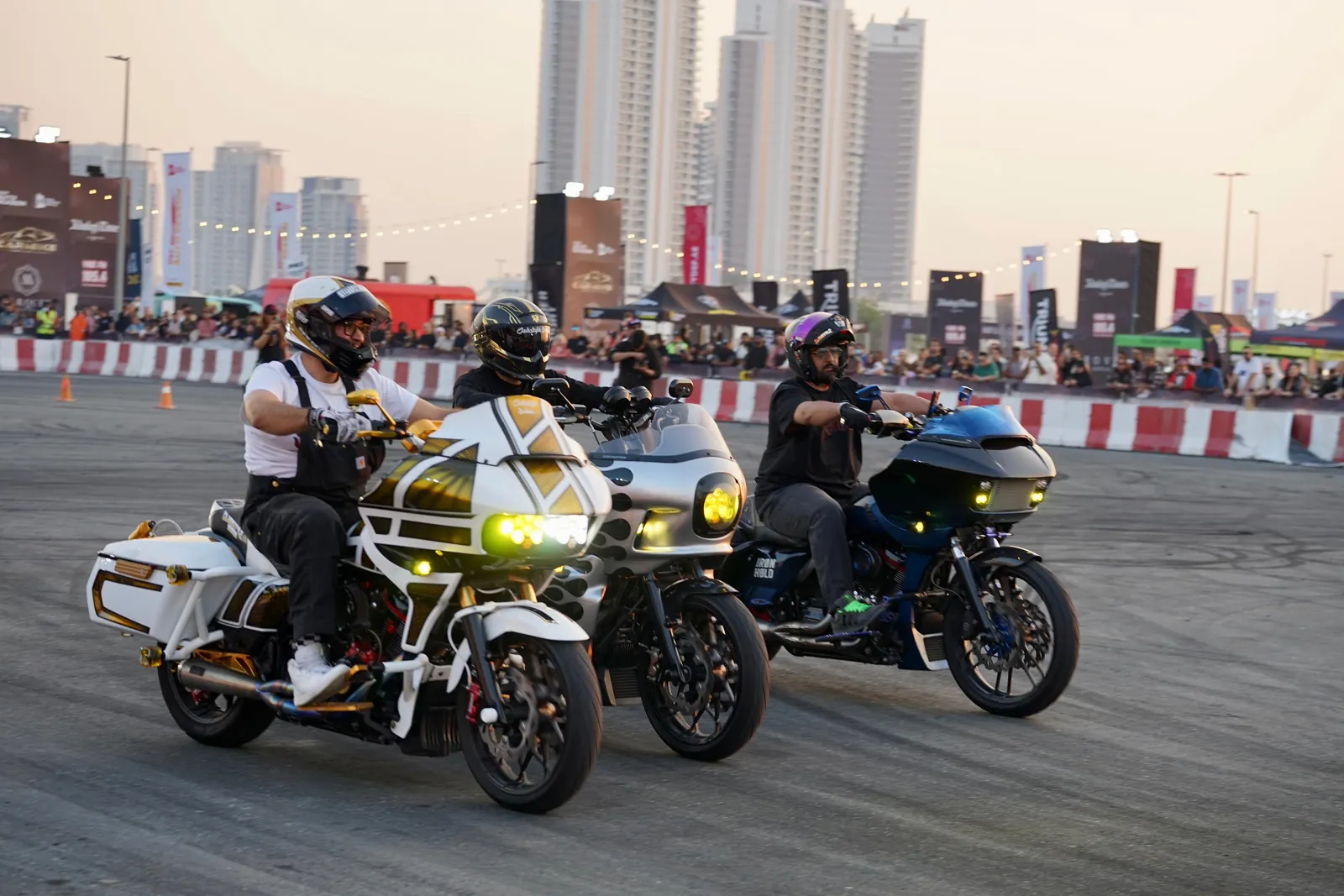 Three custom Harley baggers riding side by side at a Dubai bike show