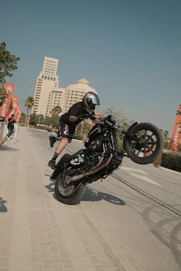 Rider holding a stoppie on a blacked-out Sportster at a Dubai street event