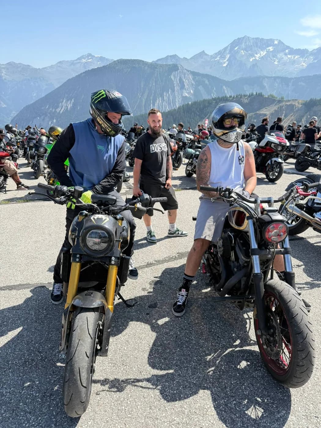 Two riders looking over their custom bikes with the snow-capped French Alps behind