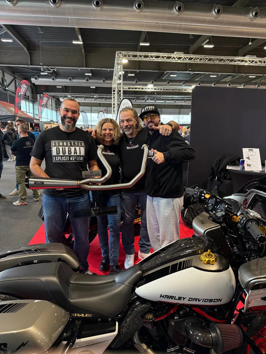 The Clubstyle Dubai crew with partners at a European motorcycle show, holding a custom Malparidos exhaust